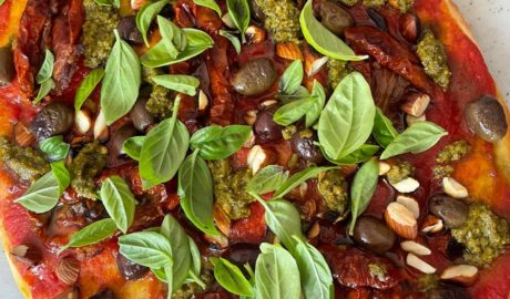 Pesto pizza with sundried tomatoes, olives, toasted almonds and basil